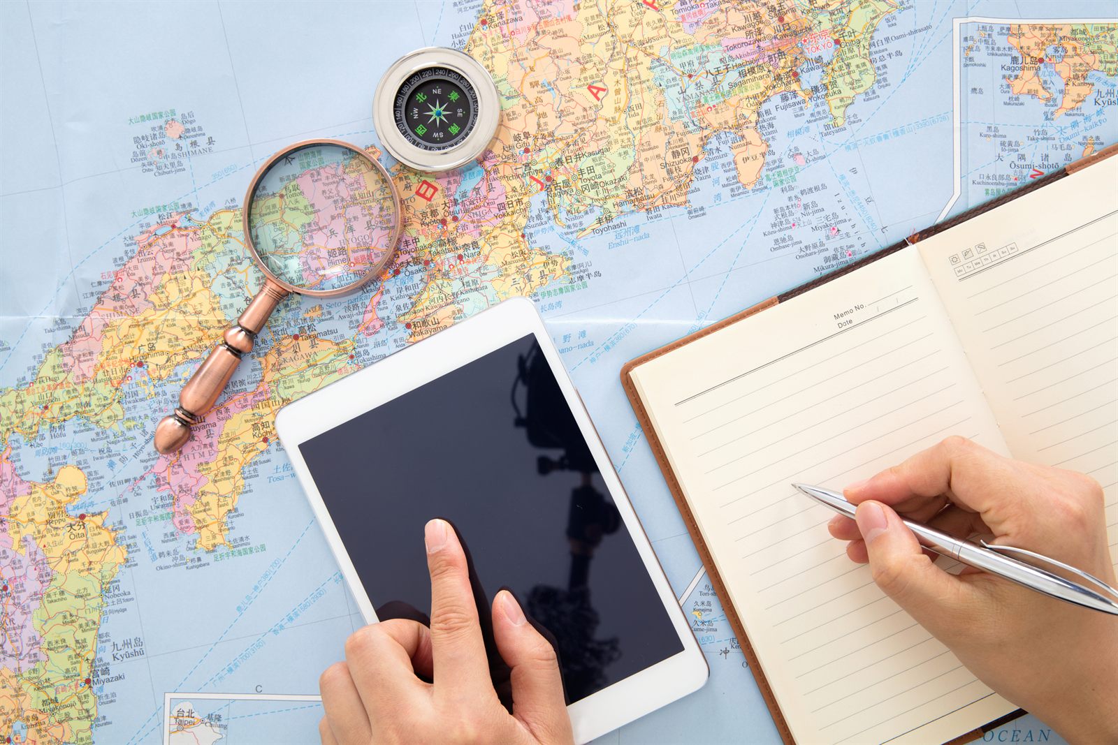 Hands with a tablet and notebook over a world map